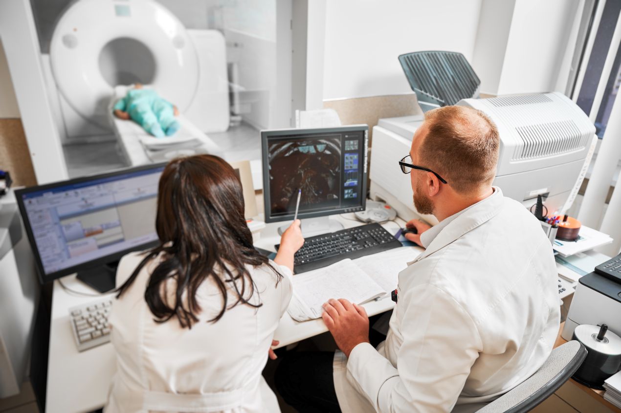 Zwei Radiologen werten MRT-Bilder am Bildschirm aus, während ein Patient in einem modernen MRT-Gerät in einer Radiologie Düsseldorf untersucht wird.