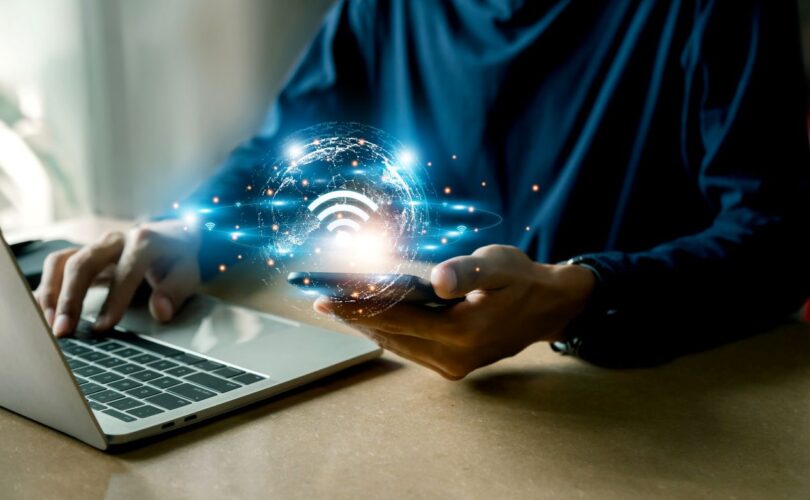 Person nutzt Laptop und Smartphone mit leuchtendem WLAN-Symbol – Symbolbild fuer MTP-basierte Netzwerktechnik und moderne Glasfaserinfrastruktur.