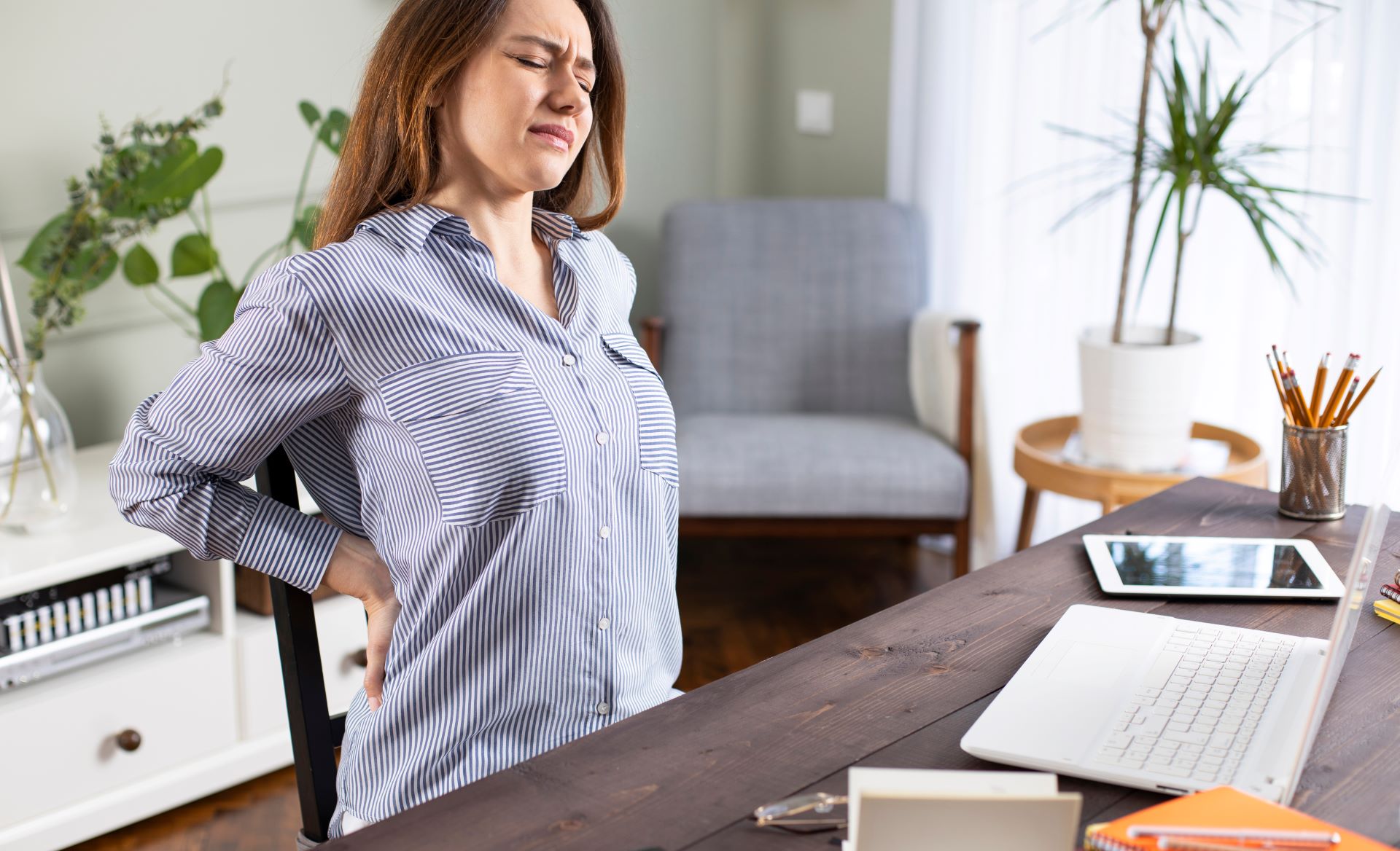 Frau mit Rückenschmerzen am Schreibtisch, ergonomische Bürostühle