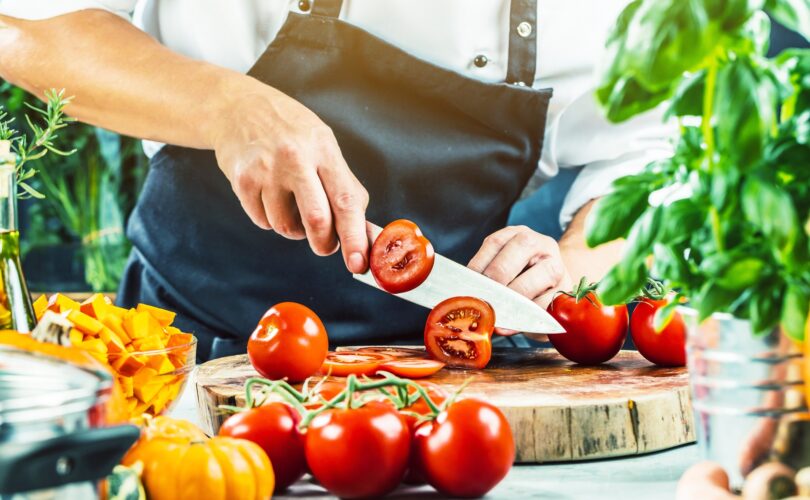 Koch schneidet Tomaten auf Holzhackbrett und Kräutern | Ceranfeldabdeckung Holz